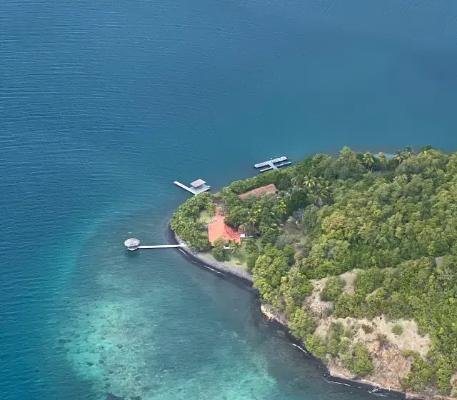 Vue aérienne de l'îlet Petite Martinique, dans la baie du Robert : pointe boisée, pontons et hauts-fonds turquoise