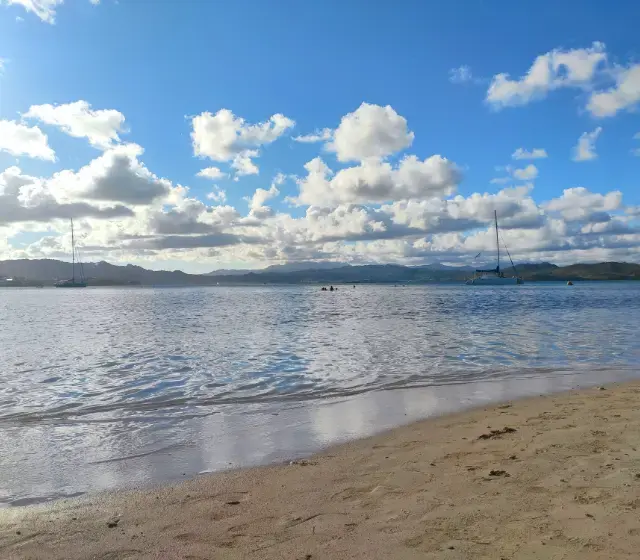 Plage de sable de l'îlet Madame au premier plan, la baie du Robert et ses voiliers au mouillage, les mornes de la Martinique à l'horizon