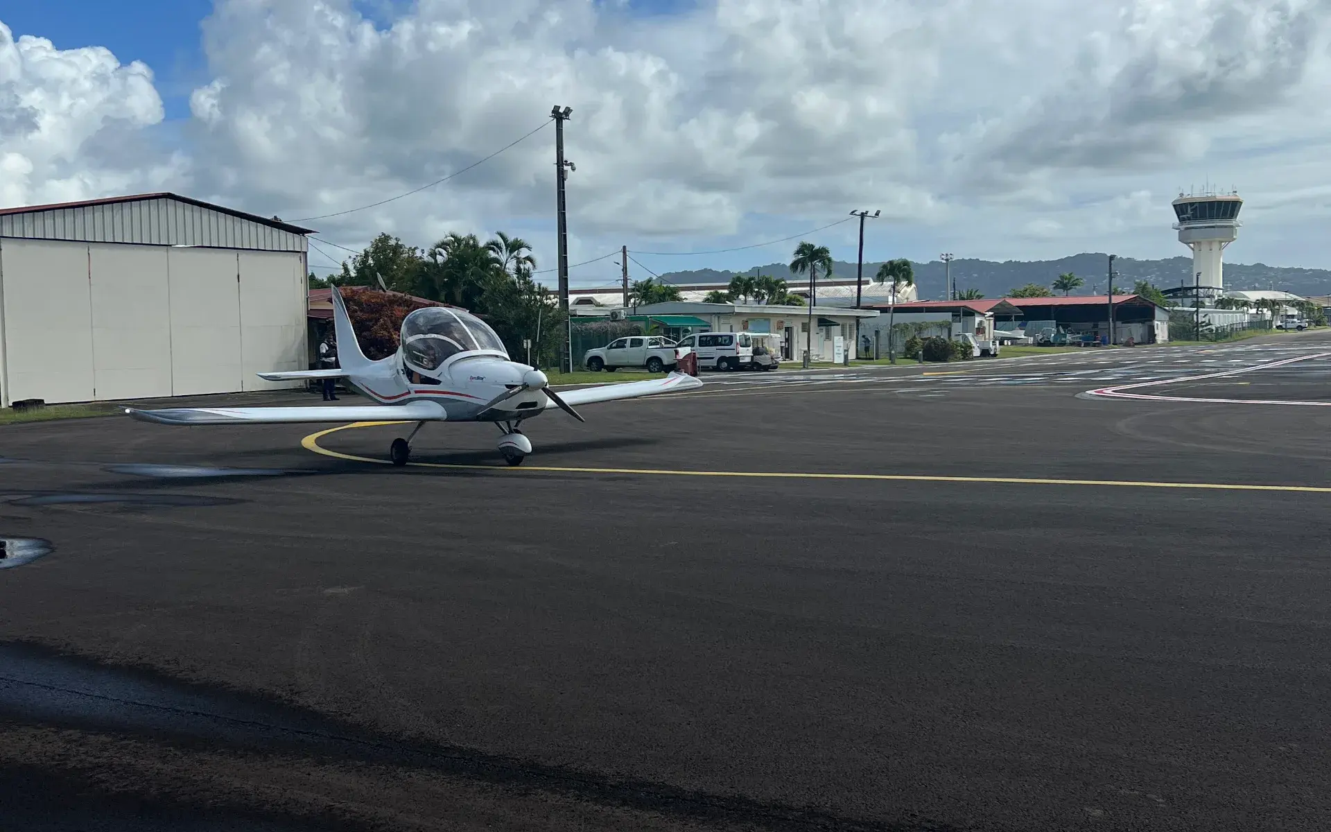 Avion léger sur le tarmac devant un hangar, tour de contrôle de l'aéroport en arrière-plan