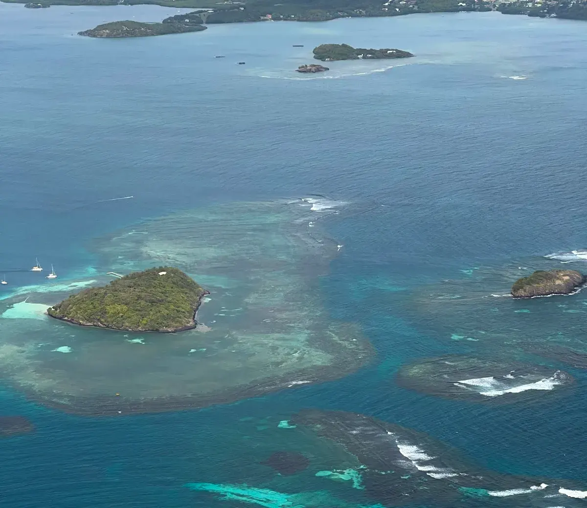 Îlets, hauts-fonds coralliens et récif vus du ciel, du turquoise pâle au bleu sombre du large